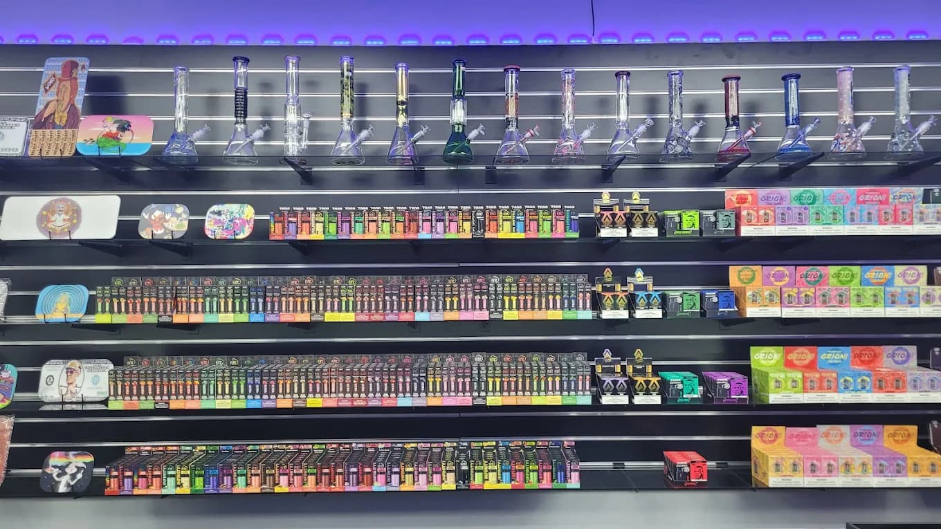 A wall of glass pipes above row after row of disposable vapes, lit by a purple cove light.