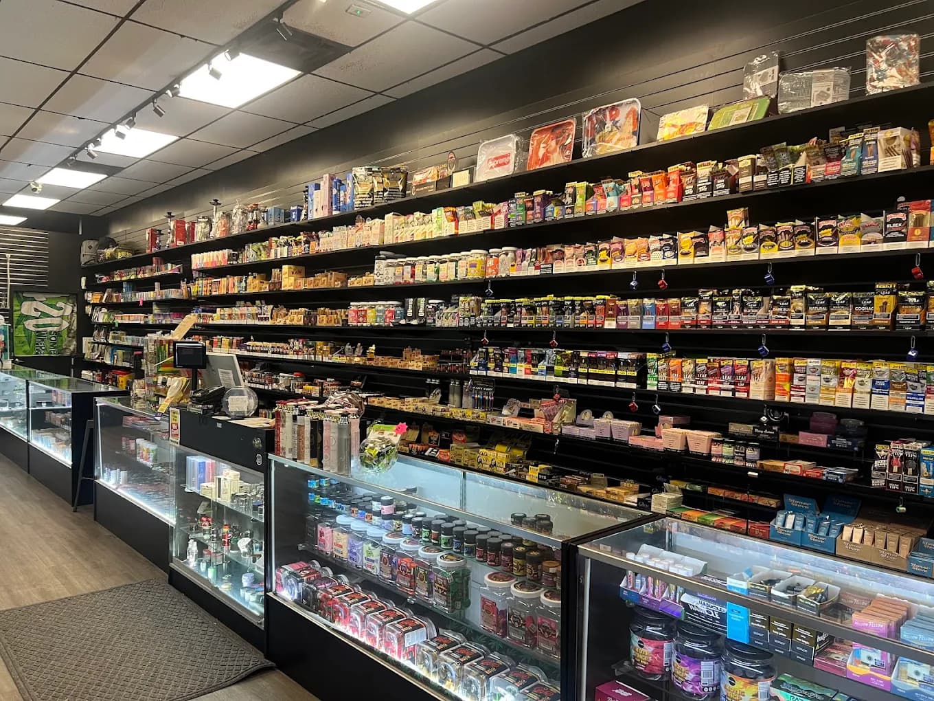 A full wall of shelves stocked with wraps, vapes and accessories above the front counter cases.