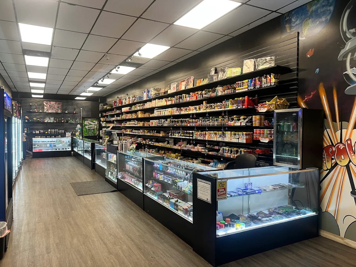 Store interior: a long wall of stocked shelves and lit glass display cases running back toward the checkout counter.